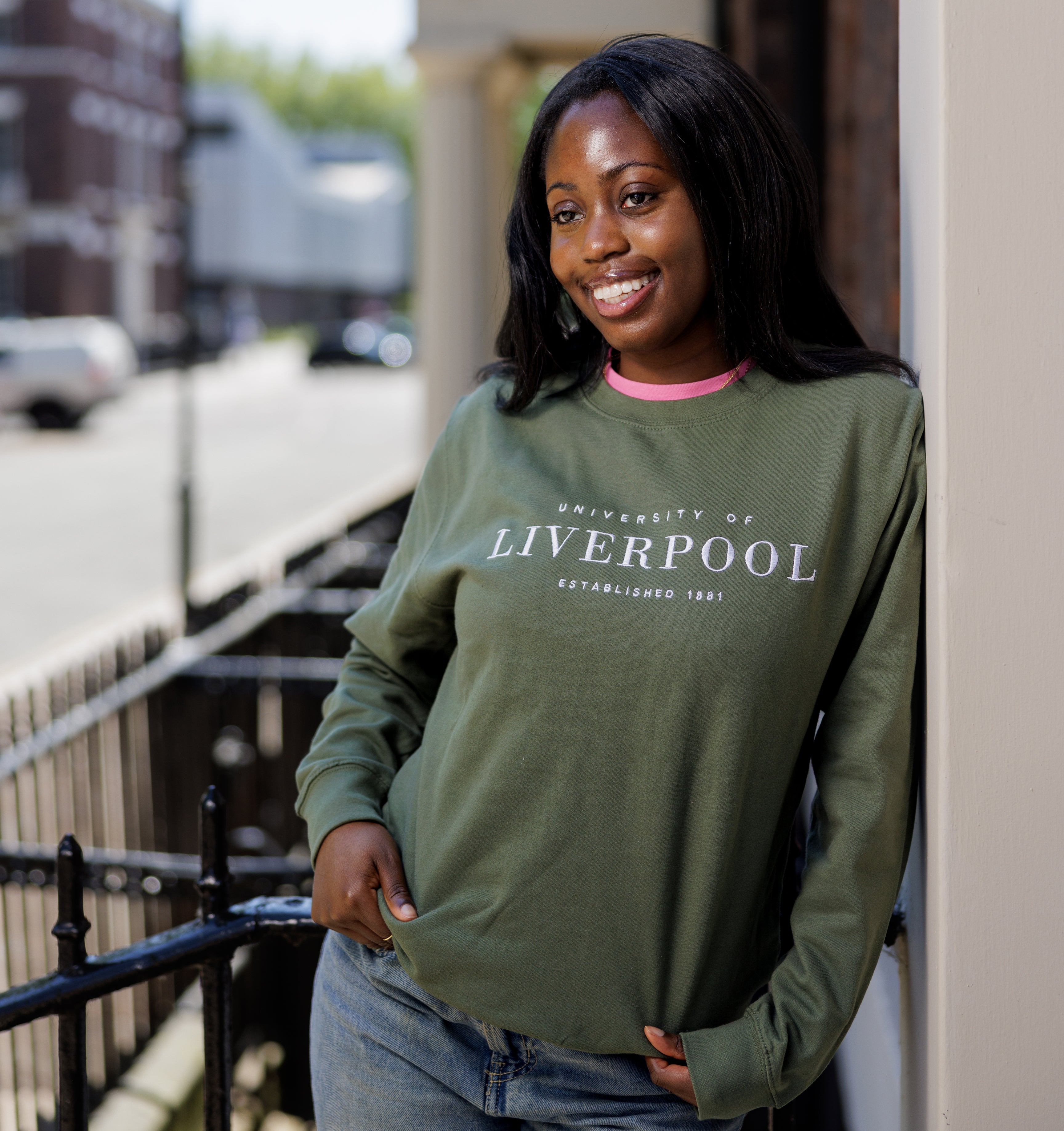 Woman wearing a green 'University of Liverpool' sweatshirt standing outdoors.